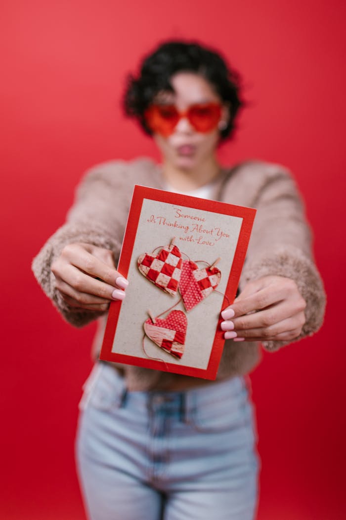 Woman in red sunglasses holding a Valentine's card on a red background.